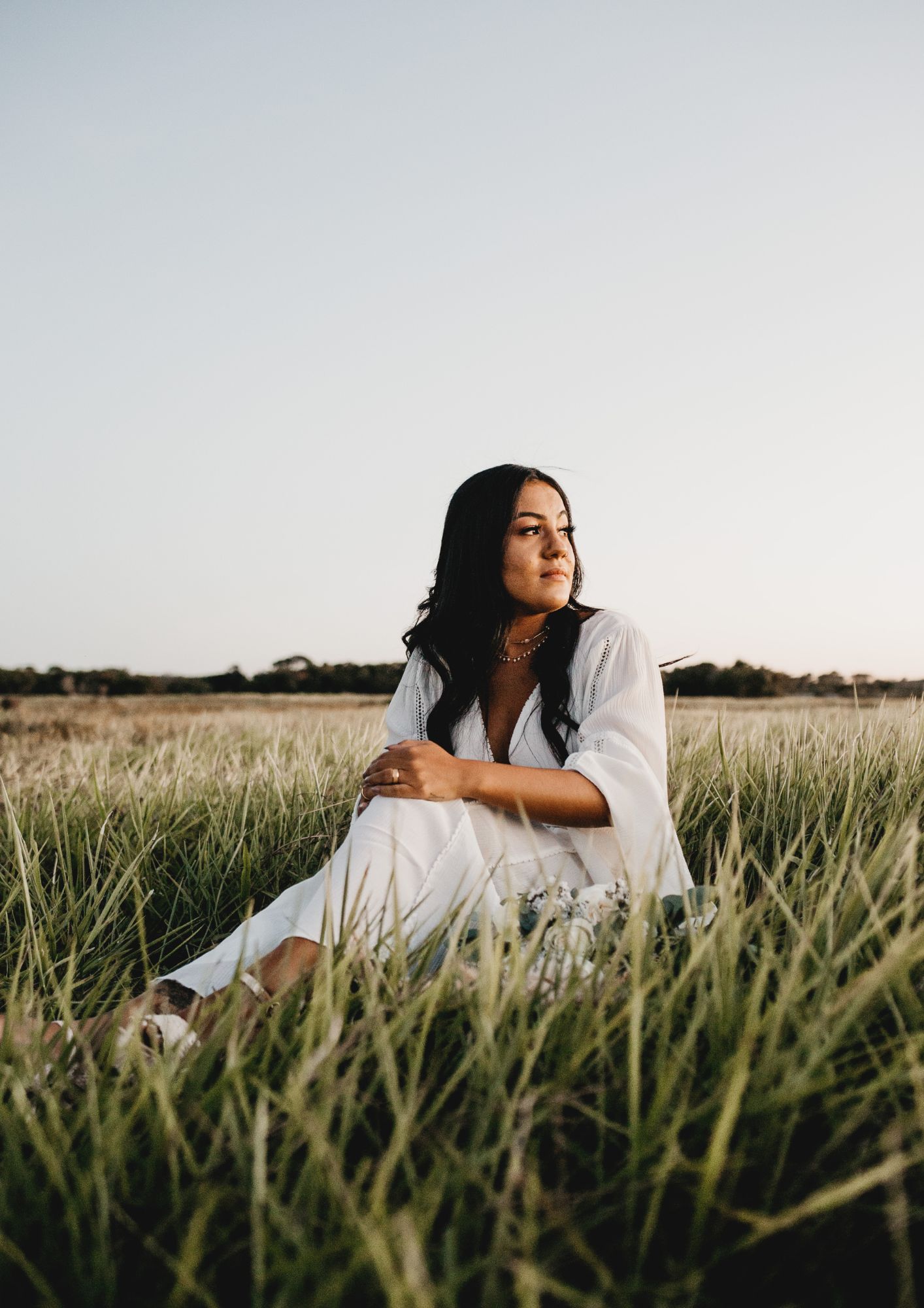 A lady in white sits in a field