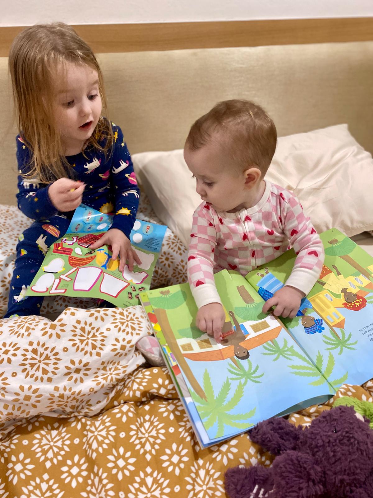 A toddler and a baby read a book together.