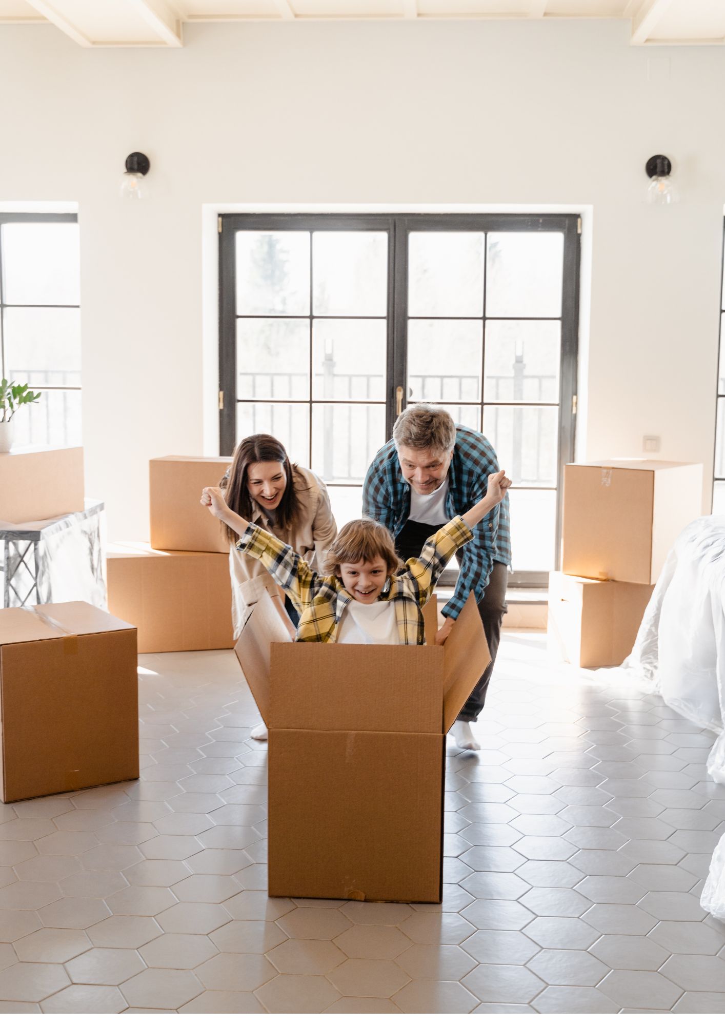Two parents push their joyful child in a cardboard box.