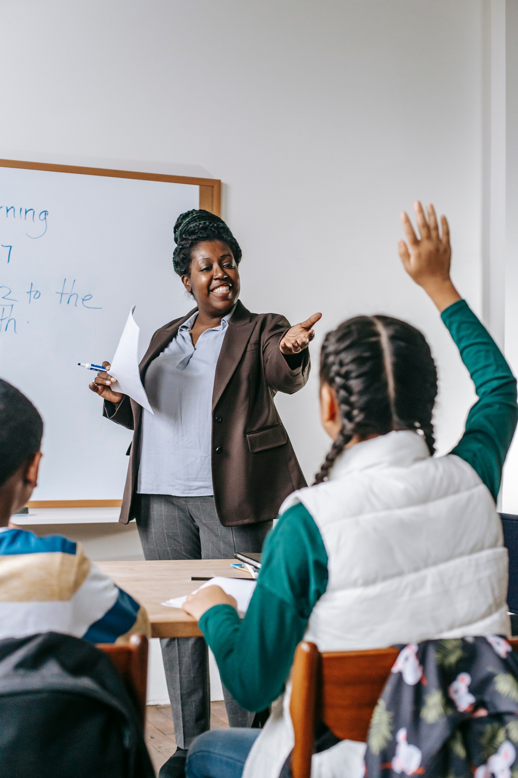 A teacher stands at the front of a classroom whilst a child raises her hand