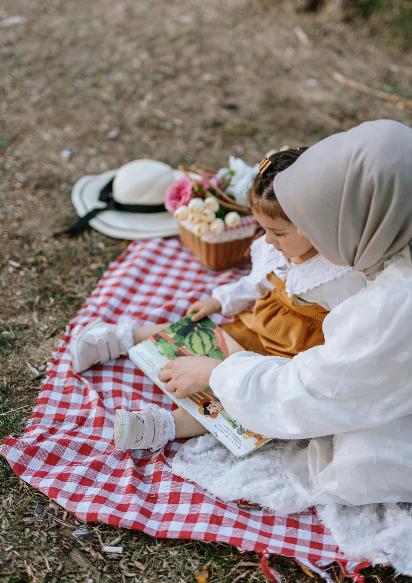 A woman and child sit on a picnic blanket outdoors and read a story about food