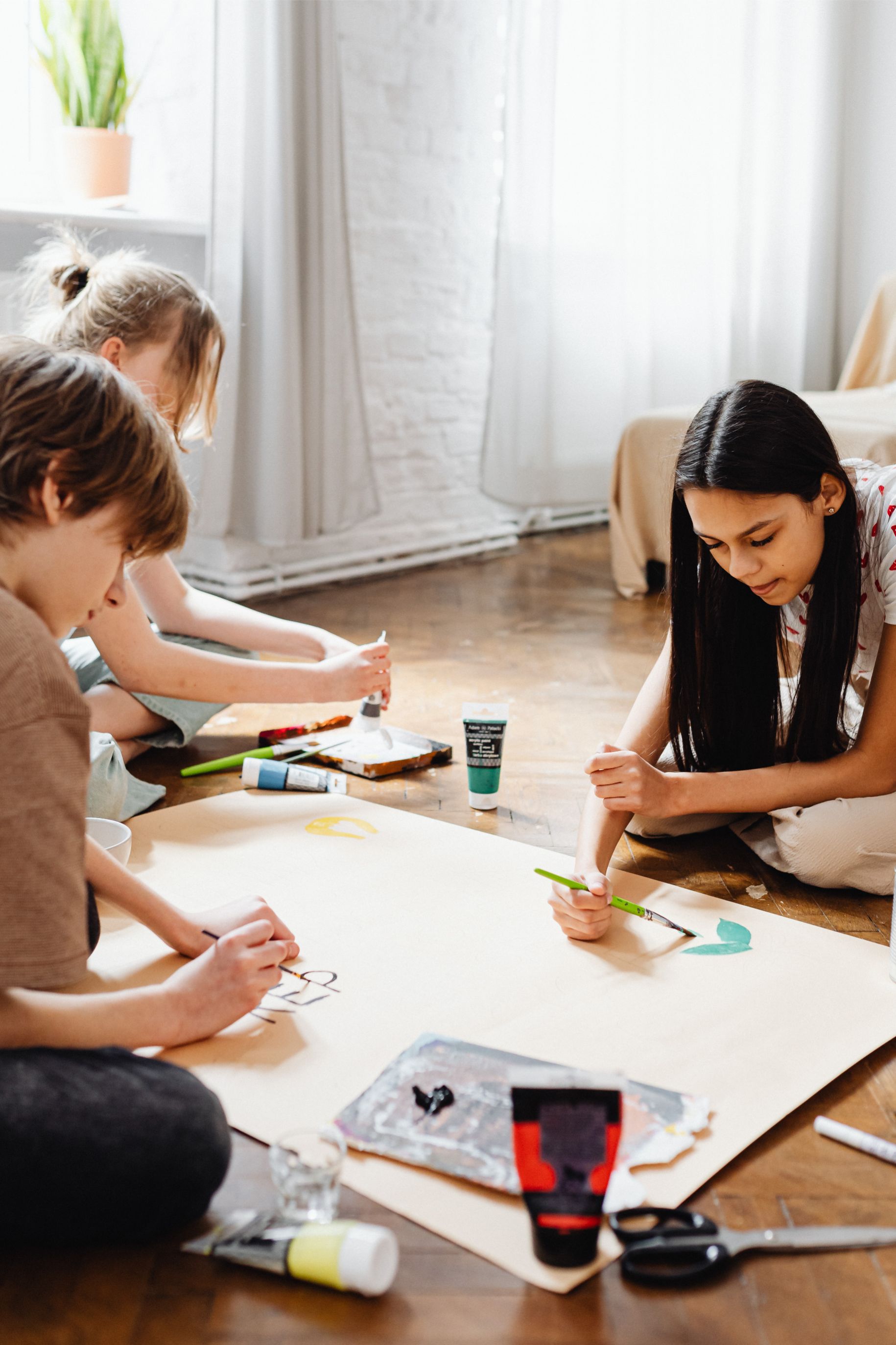 A group of tweens complete a large-scale painting project together seated on the floor