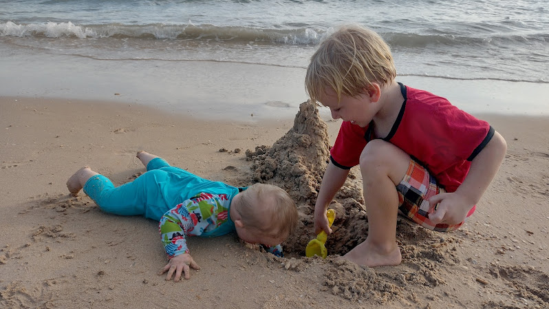 Two young children dig a hole at the beach