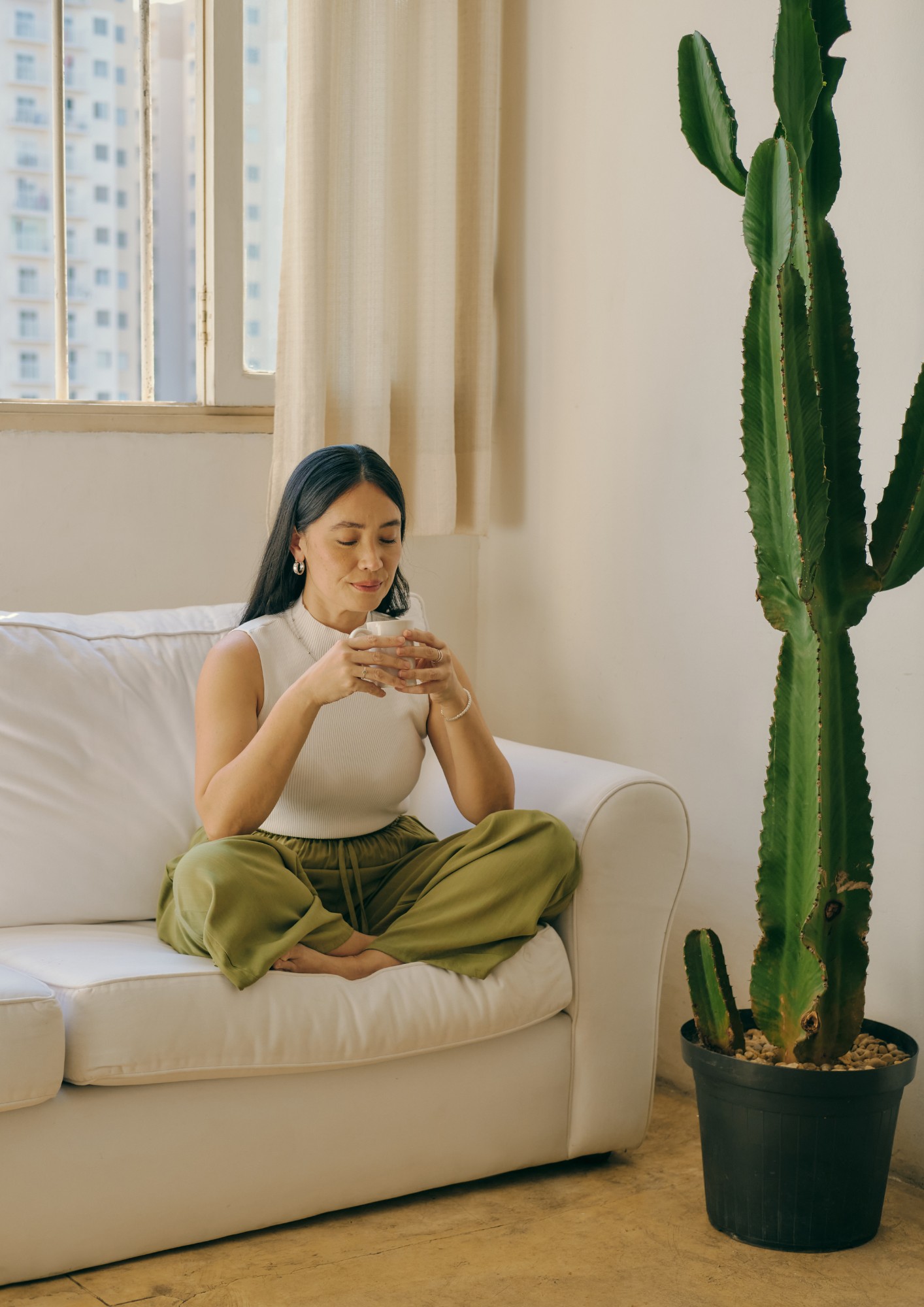 A lady sits on a couch by a large cactus