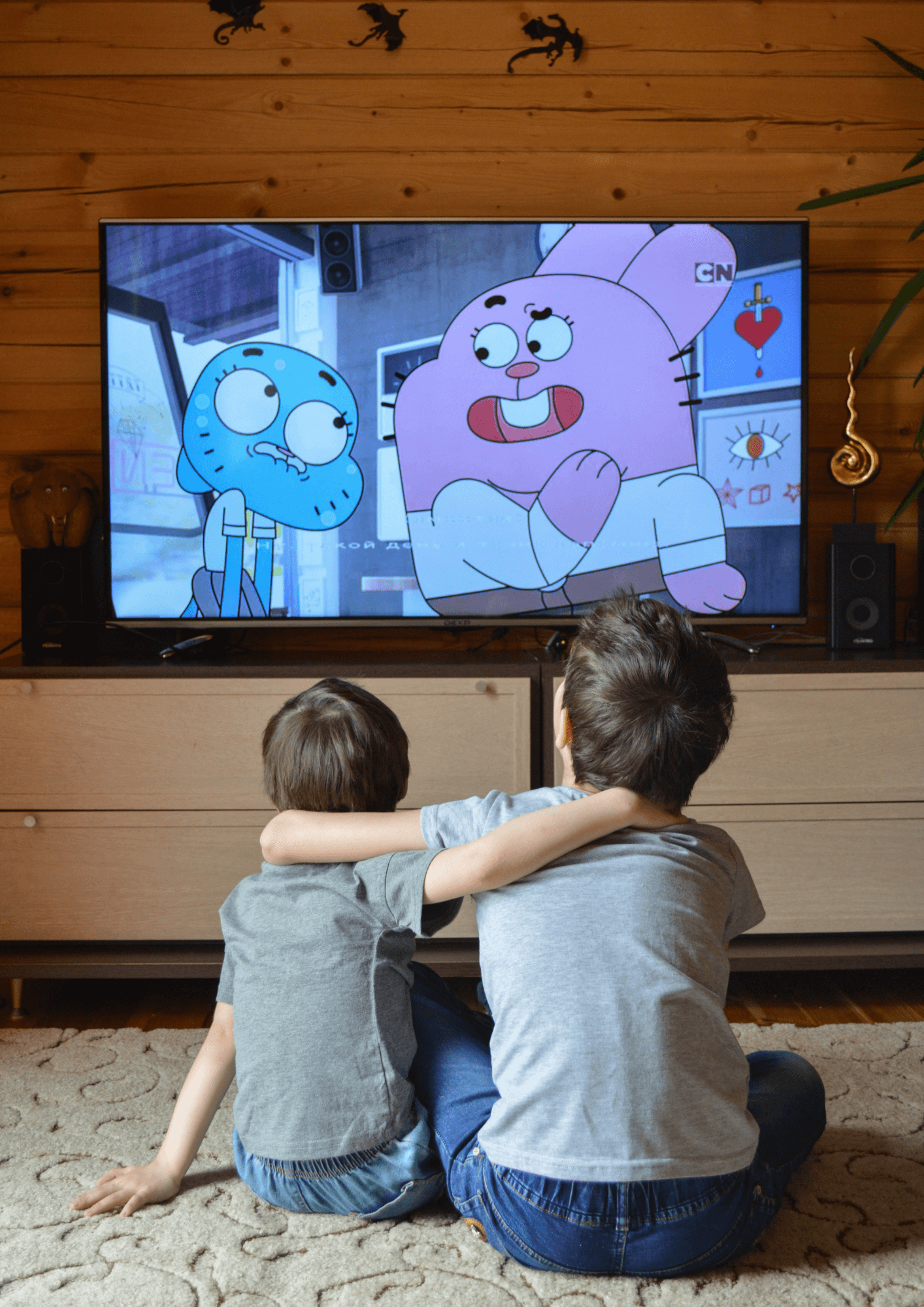 Two young white children sit together and watch an animated TV show