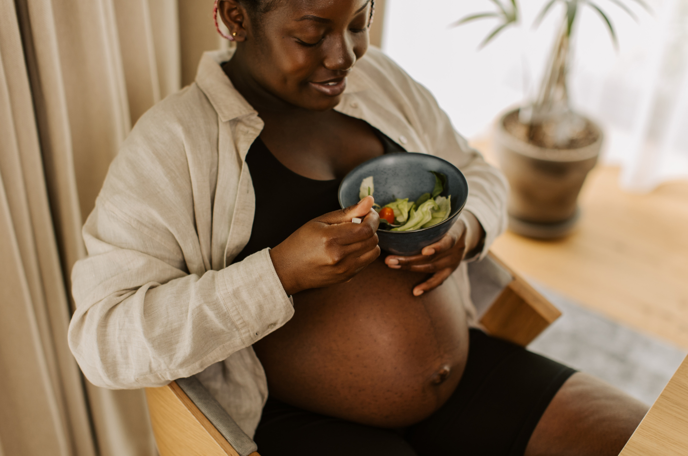A Black pregnant woman eating vegetables
