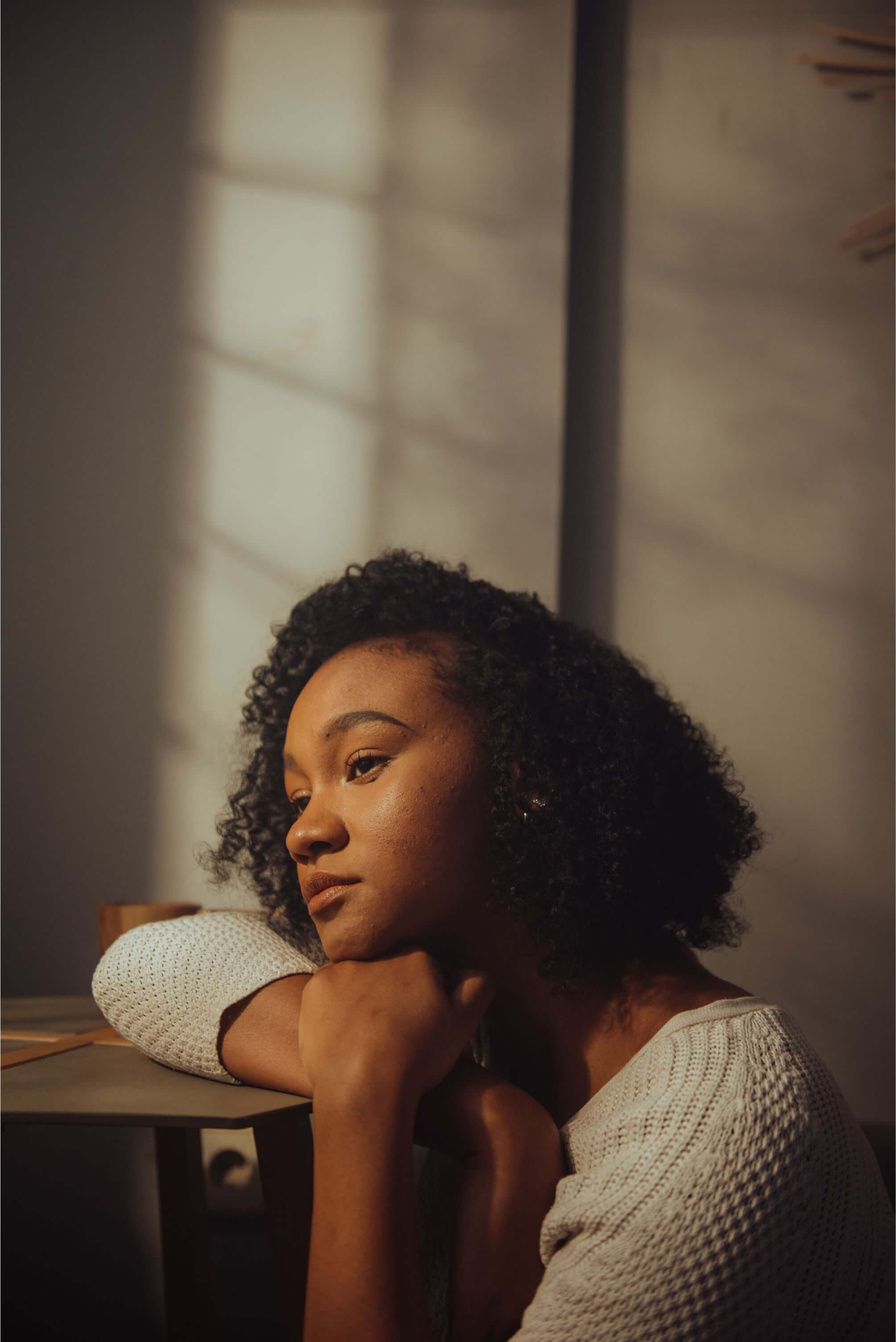 A Black woman staring sadly into space, her head rested on her hands