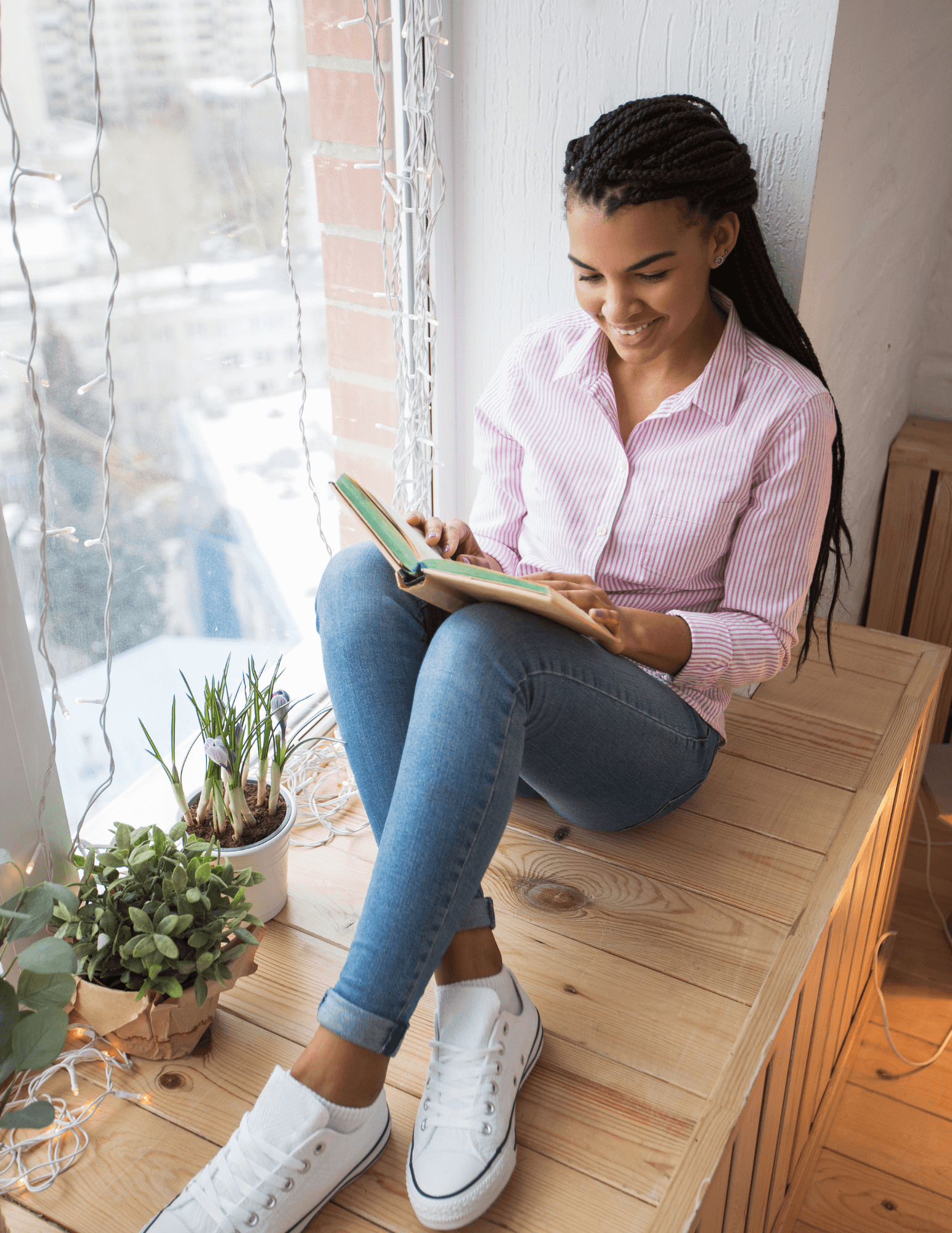 A black woman sitting in a window reading nook and reading a book