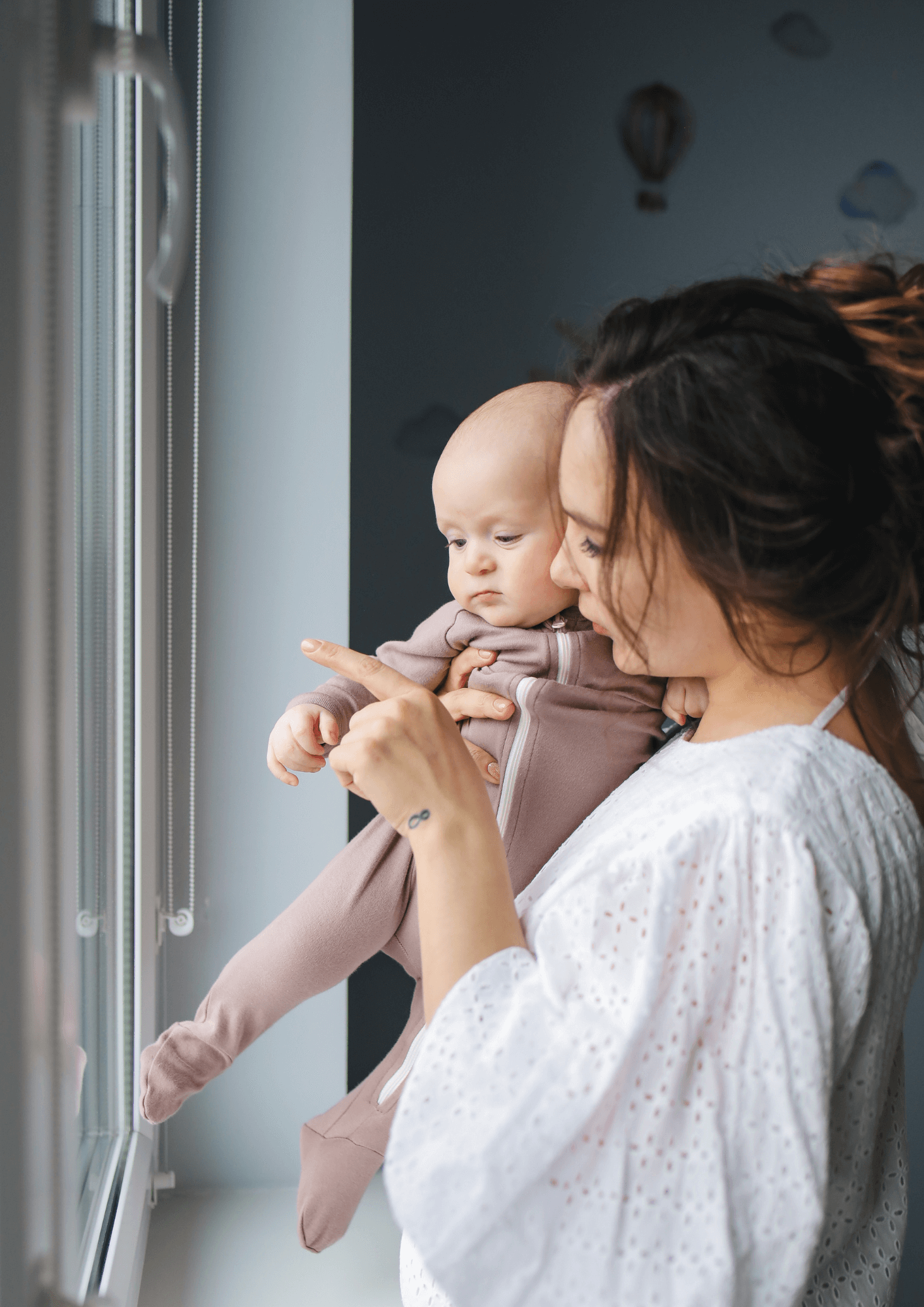 A white woman and her baby stand together looking out of a window