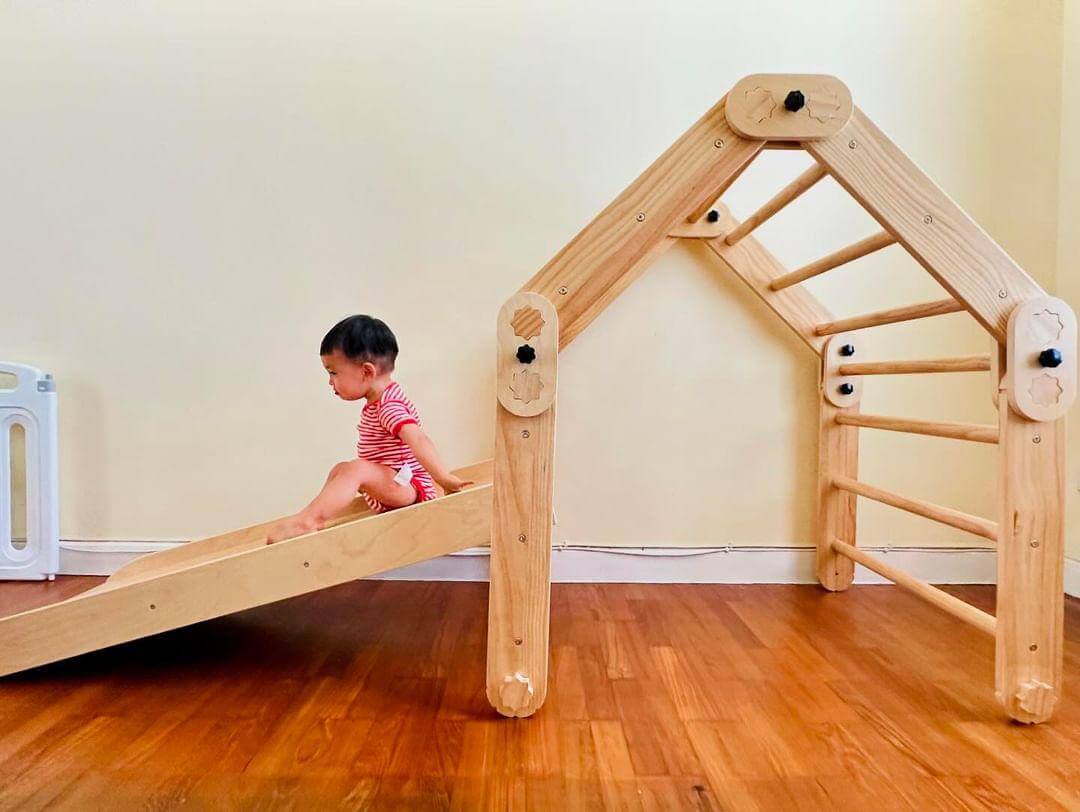 A toddler on an indoor wooden climbing frame and slide