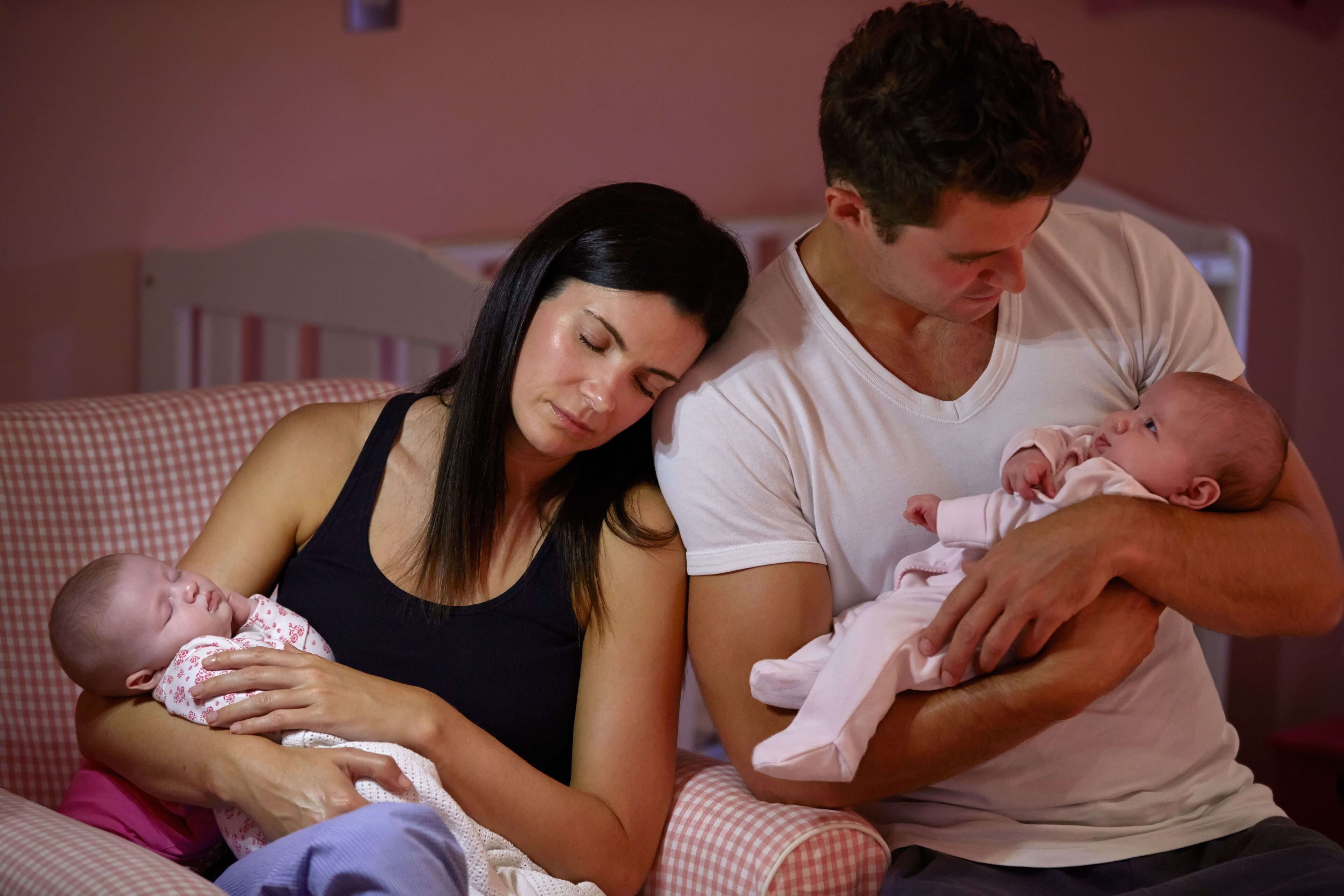 A white man and woman cradling newborn babies. The woman has her eyes closed and rests her head on the man's shoulder.