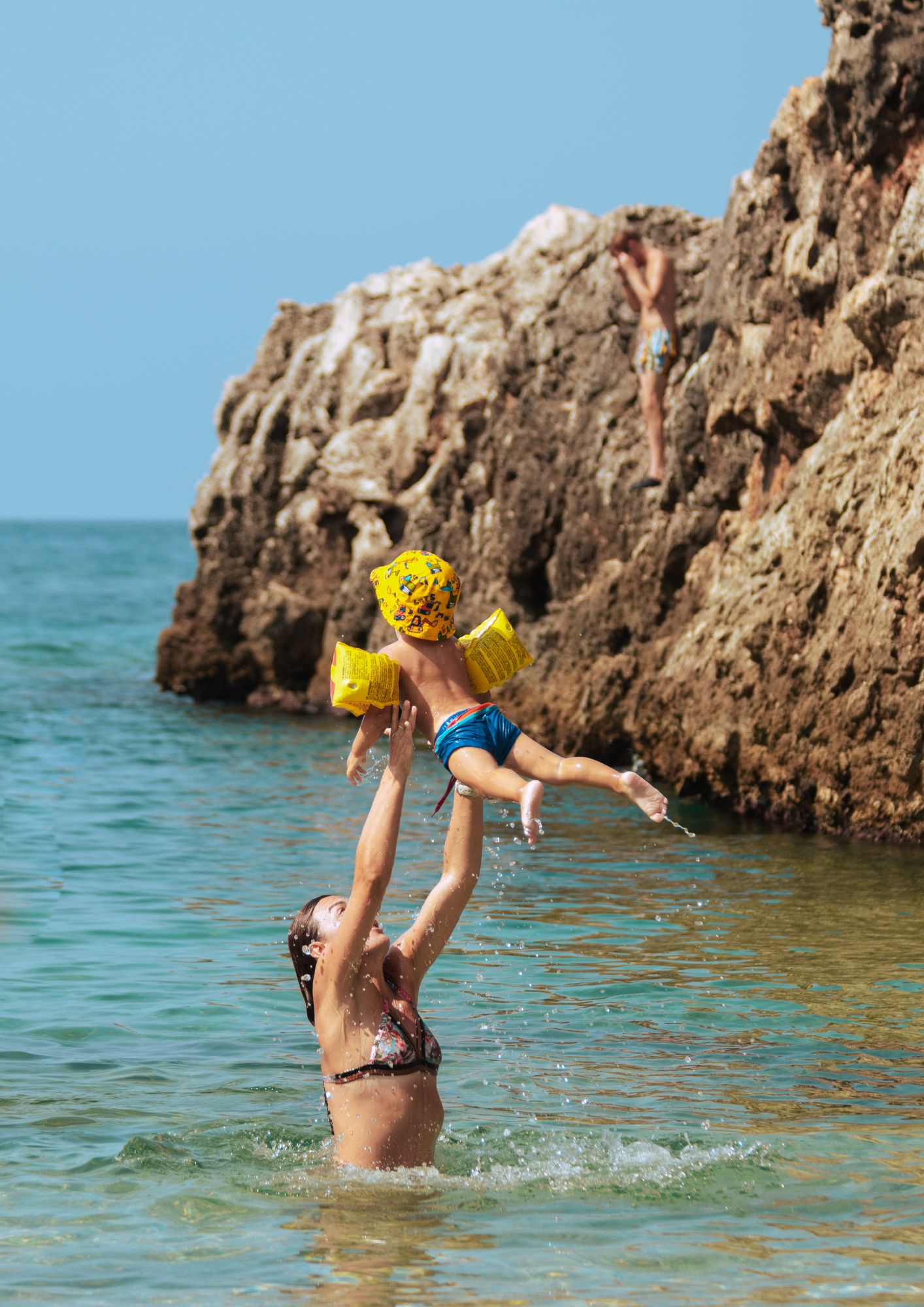 A mother in the sea throws their child in the air. 