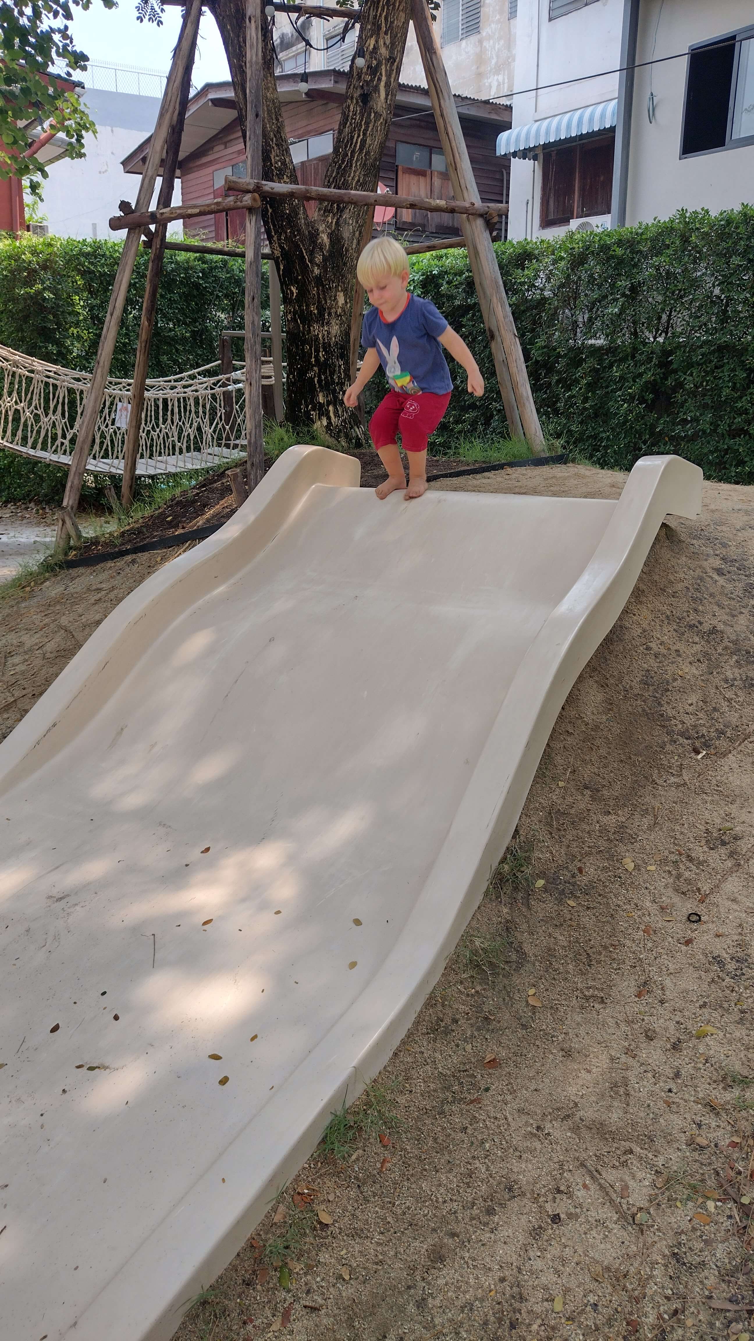 A White toddler playing on a slide at an outdoor cafe