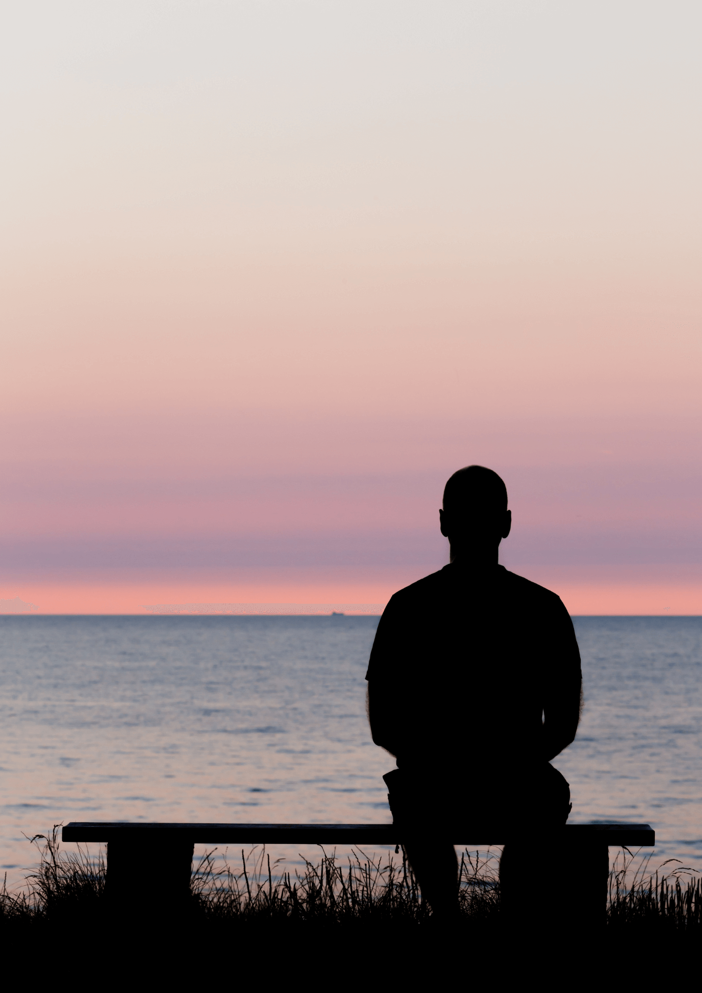 The silhouette of a man sitting alone in front of the ocean at sunset