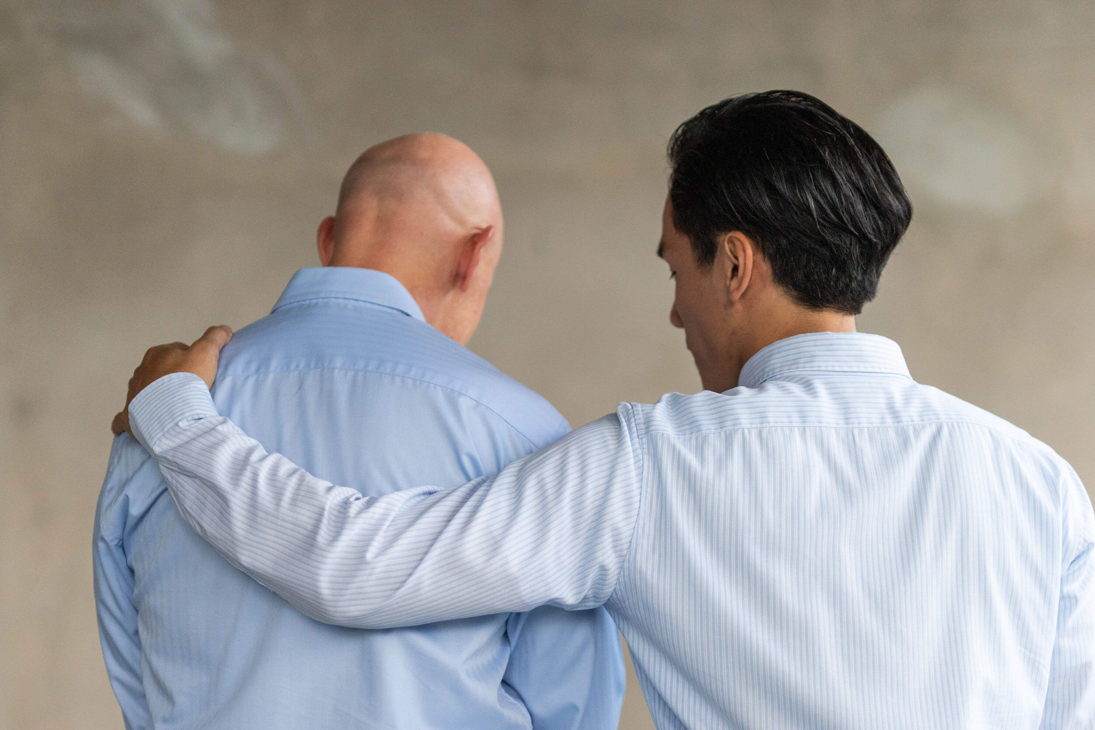 From behind, two men, one with his arm around the other