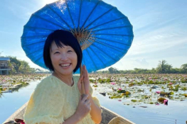 A Chinese woman sitting in a boat on a lotus pond and smiling