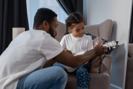 A dad teaching his daughter how to play guitar