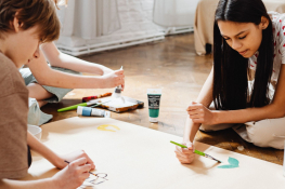 A small group of tweens work on a large-scale painting project while seated together on the floor