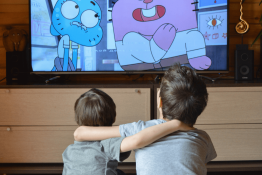 Two young white children sit together and watch an animated TV show