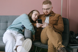 A couple sit on a couch looking at their phones