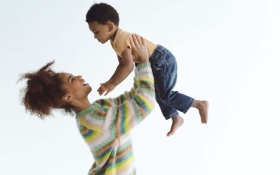 A Black woman lifting her son above her head by holding him under his armpits