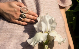 A close-up of a woman's pelvic region. She is dressed in a beige top and is holding a white flower in front of her in line with her uterus
