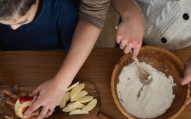 A parent and their two kids prepare ingredients for an apple pie