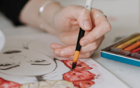 A white person holds a paintbrush and works on a painting