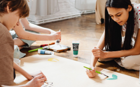 A small group of tweens work on a large-scale painting project while seated together on the floor