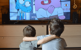 Two young white children sit together and watch an animated TV show