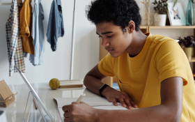 A Black teen boy studies at his desk