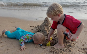 Two young children dig a hole on the beach