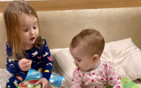 A toddler and a baby look at a book.
