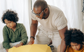 A father and two children try to shut a suitcase.