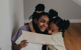 Two sisters in tears hug each other sitting on the stairs