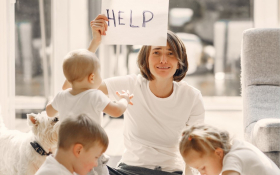 A parent surrounded by children holds up a sign asking for help.