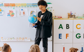 A teacher holds a globe at the front of a classroom